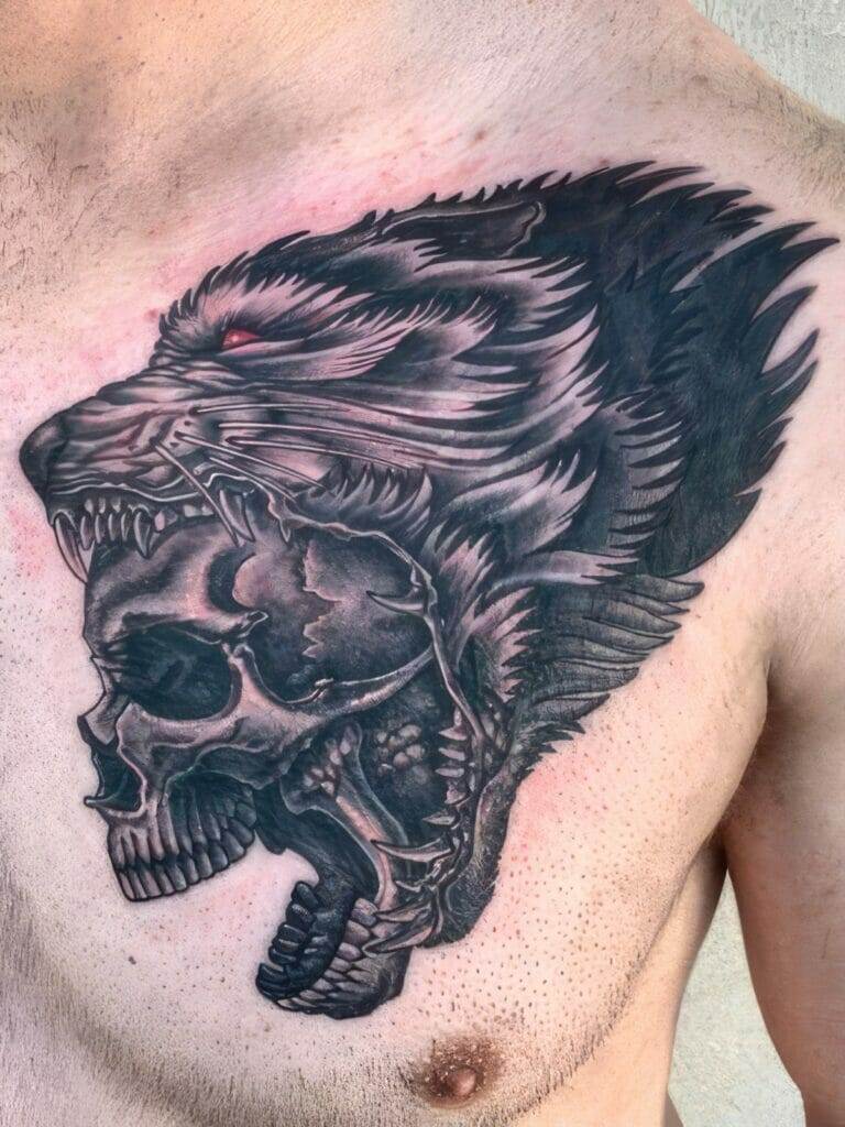 A detailed black tattoo on a person's chest depicts a roaring lion's head blending into a skull.