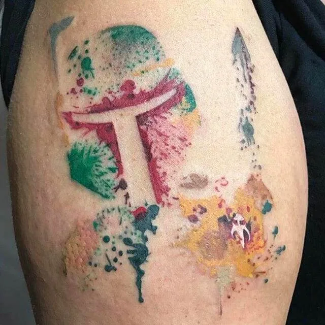 A colorful, abstract tattoo featuring a design resembling a helmet from the Star Wars universe is on a person's upper arm.