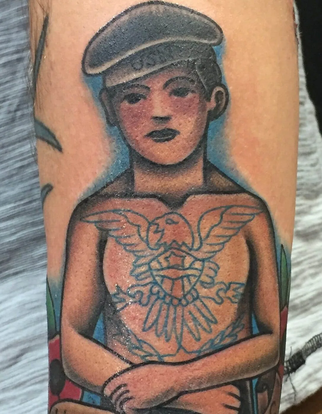 Tattoo of a person wearing a hat, with a large eagle and shield tattooed on their chest.