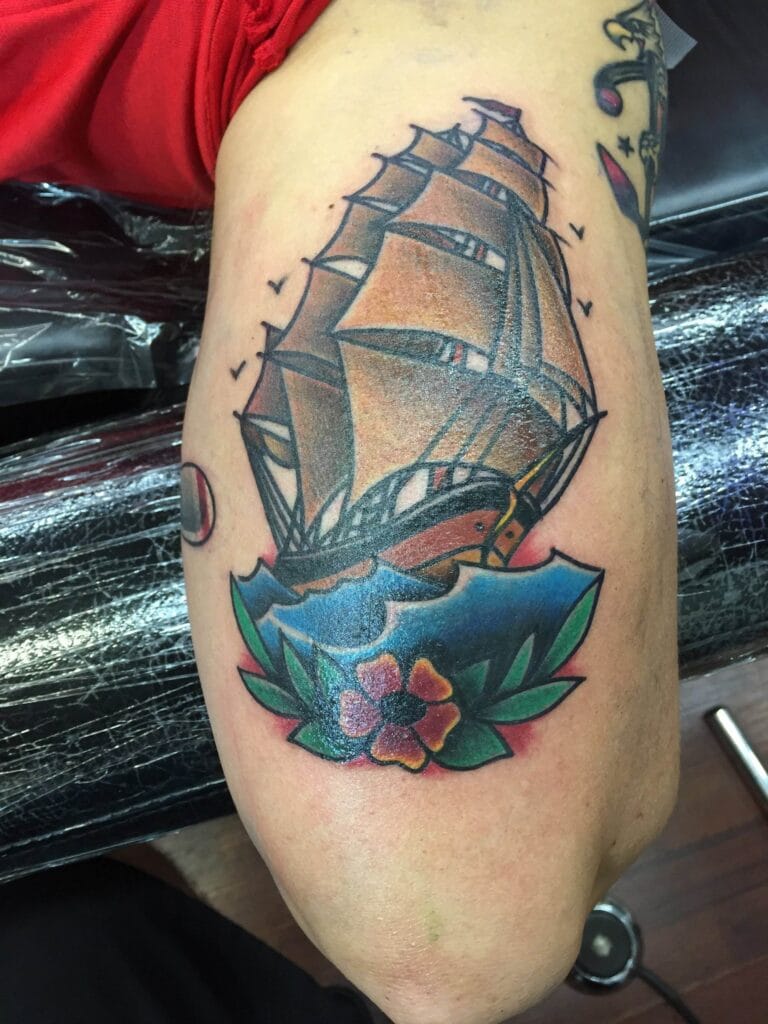 A traditional-style sailing ship with brown sails above a colorful flower and leaves.