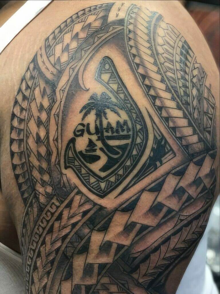 A detailed tattoo on an arm featuring intricate designs around a central emblem with the text "Guam" and a palm tree.