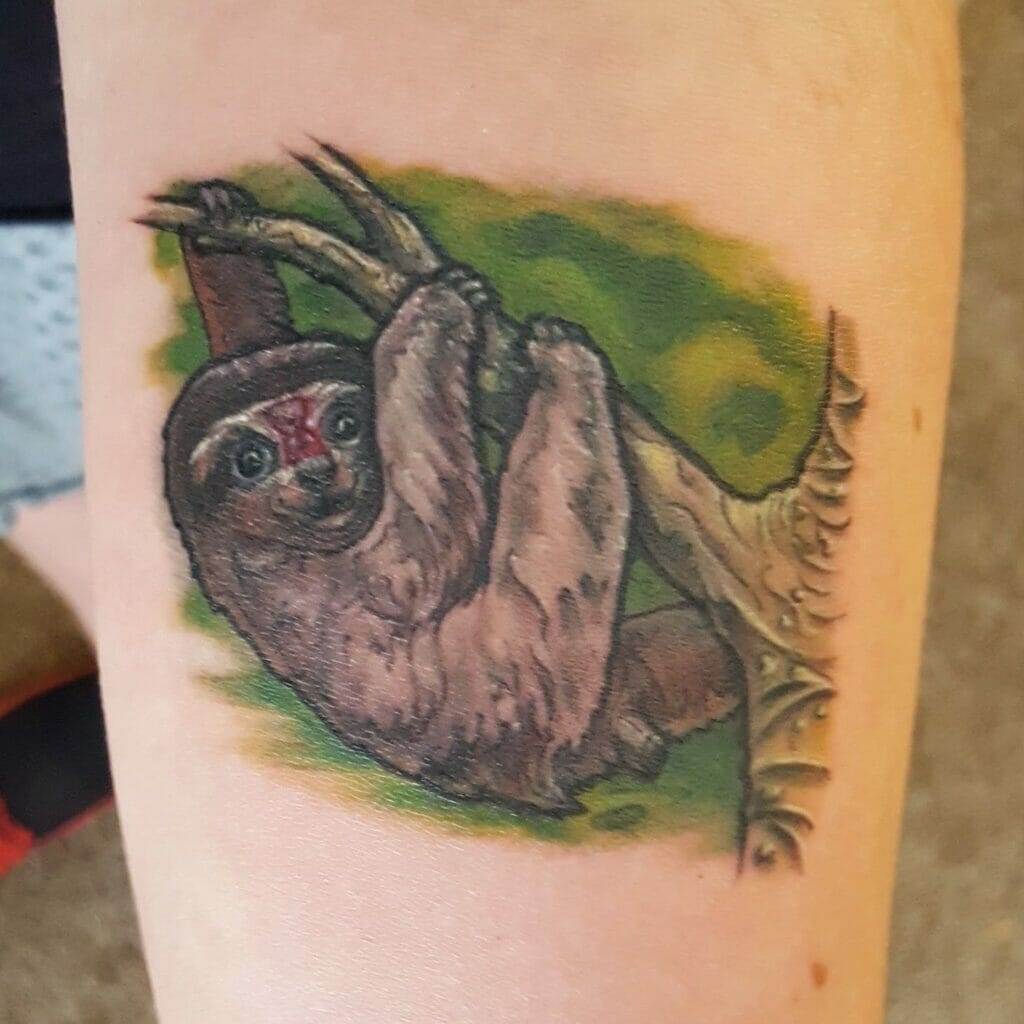 A tattoo of a sloth hanging from a tree branch is depicted on skin. The sloth appears detailed with a blend of green and brown colors for background and shading.