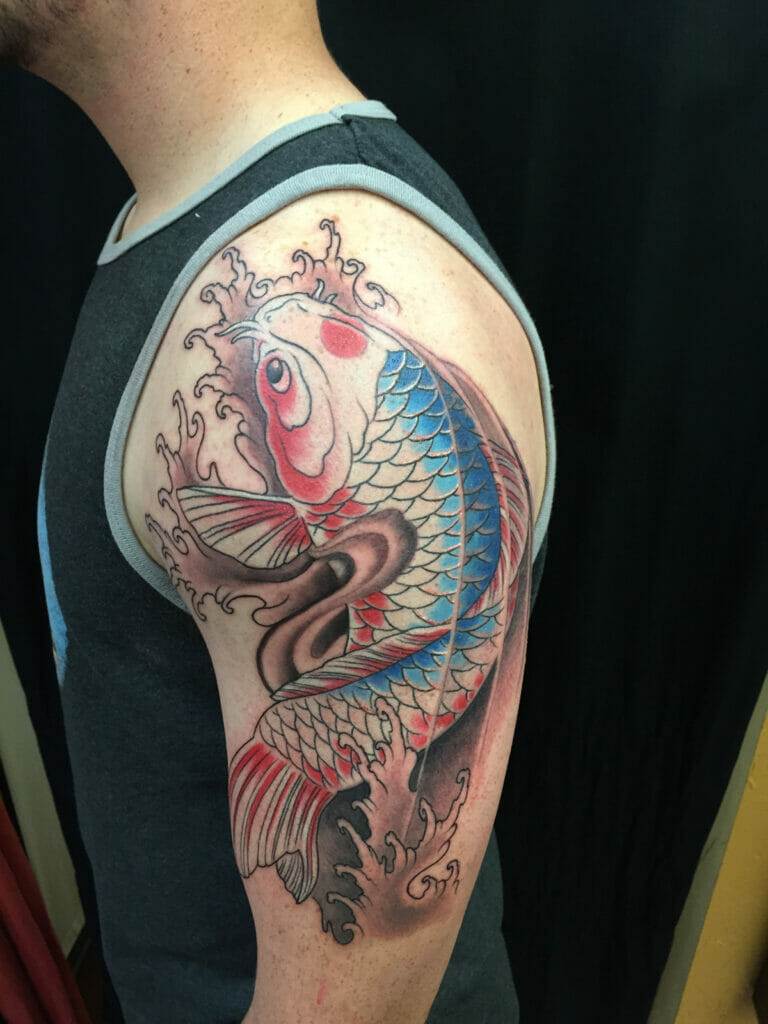 A person's upper arm tattoo depicting a colorful koi fish with blue, red, and white scales, surrounded by water elements.