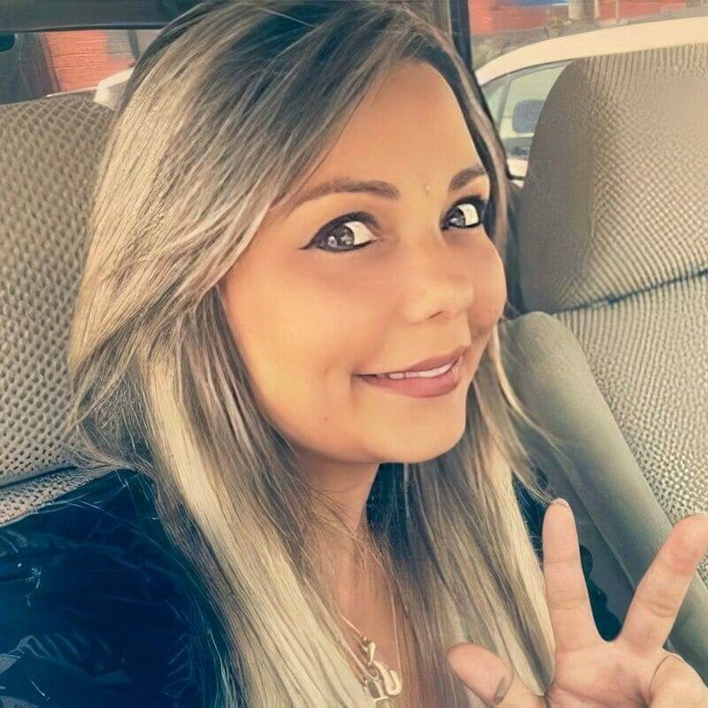 Woman with long blonde hair smiling and making a peace sign inside a car.