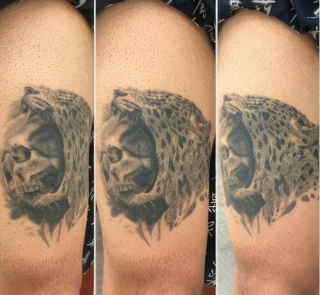 A tattoo of a leopard's head, mouth open, and superimposed with a human skull on the inner thigh of a person.