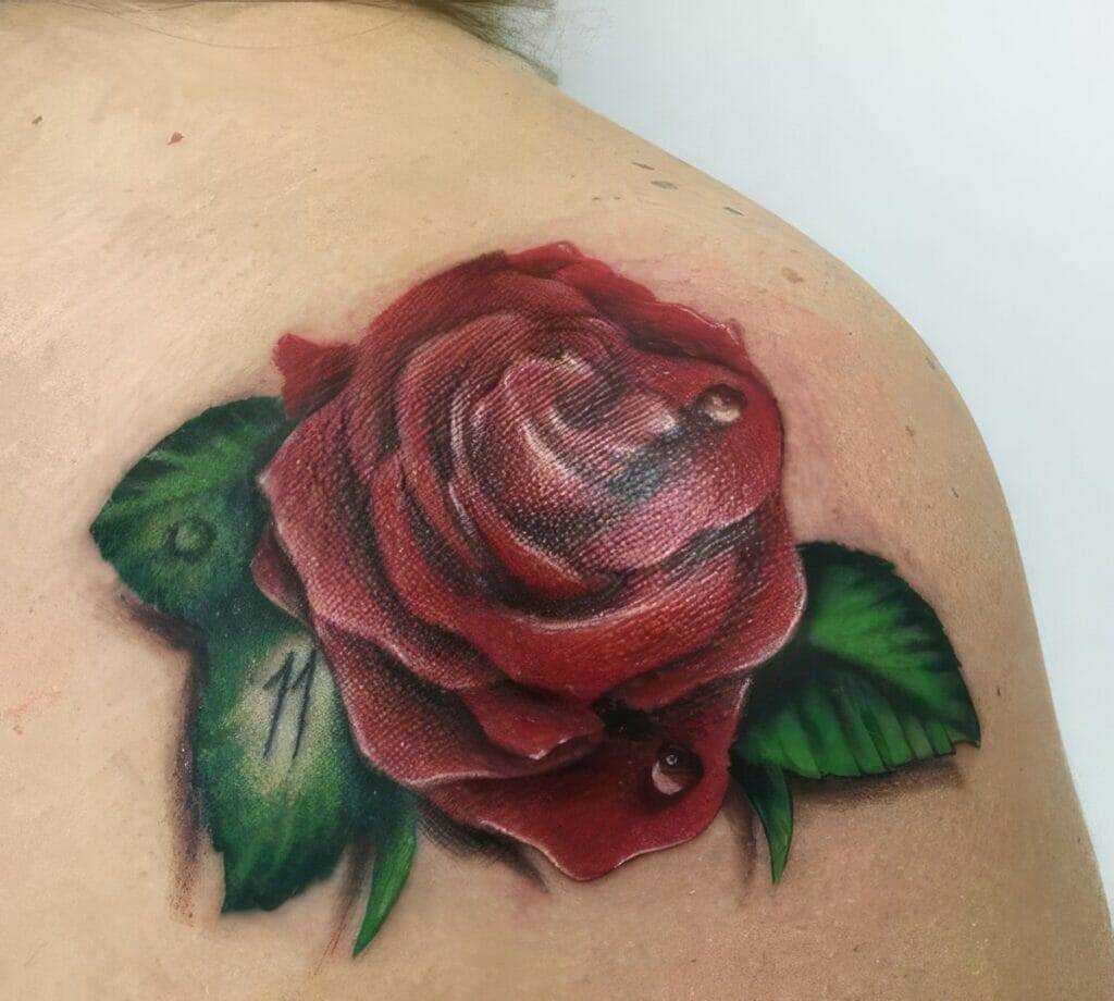 A realistic tattoo of a red rose with green leaves on a person's shoulder.