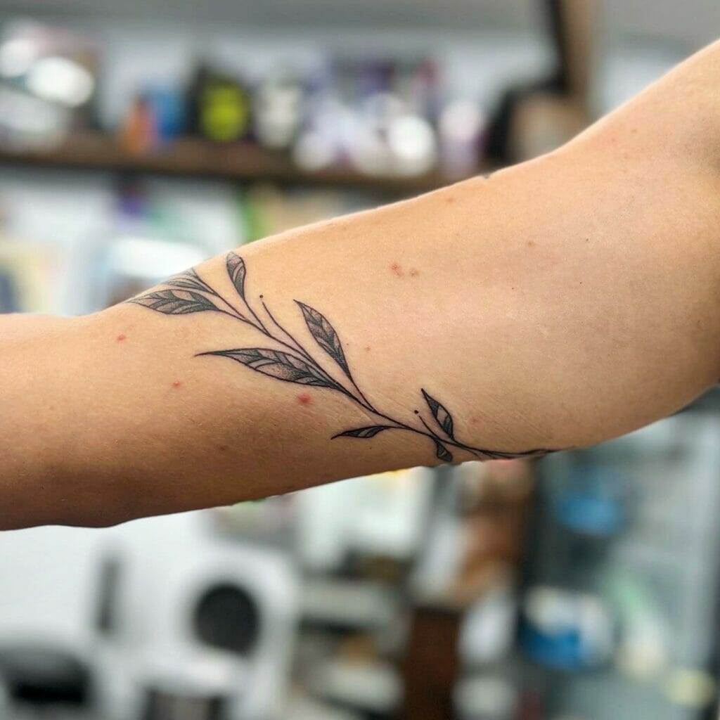 A close-up image of a person's arm with a minimalist tattoo of a leafy branch.