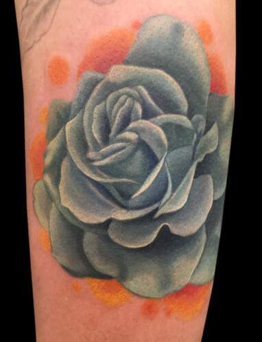 Tattoo of a green rose with orange accents on a person's skin.