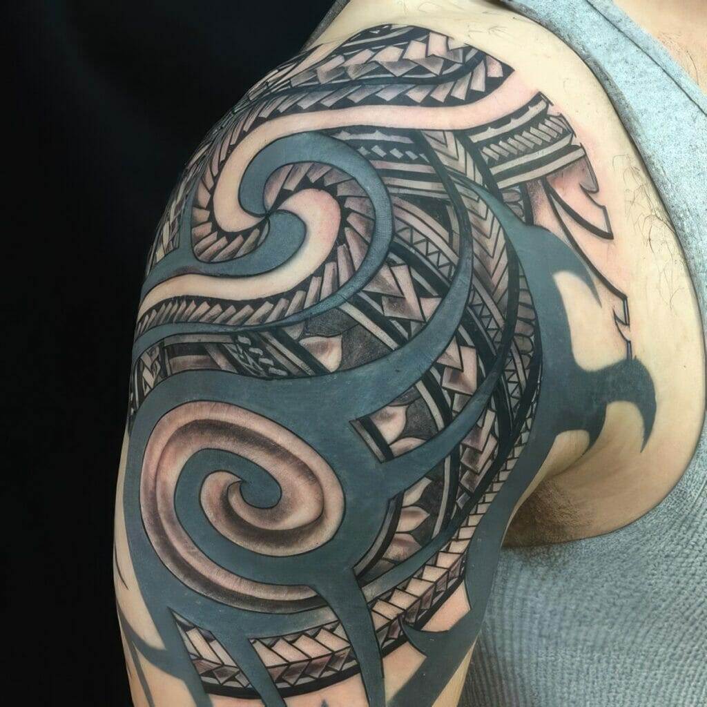 A close-up of a person's upper arm featuring a detailed tattoo with intricate tribal patterns and swirling designs. The person is wearing a sleeveless gray shirt.