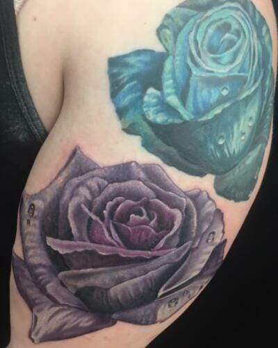 A close-up view of an arm with two large, detailed rose tattoos in shades of blue and purple.