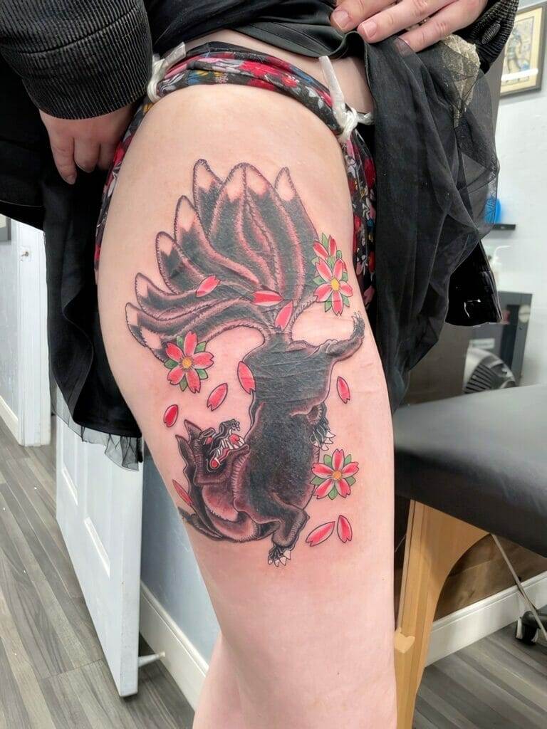 A tattoo of a black panther with red flowers and petals is displayed on a person's thigh, standing in what appears to be a tattoo parlor.