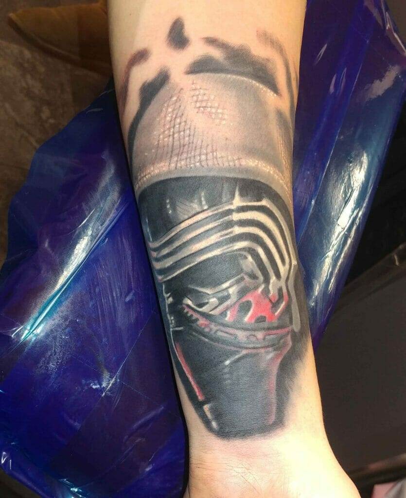 Forearm tattoo featuring a detailed image of a helmet reminiscent of Kylo Ren from the Star Wars series, depicted with black, grey, and red ink.