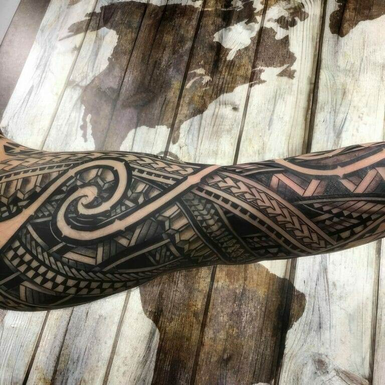 A forearm with a detailed black geometric tattoo design sits over a wooden surface with a world map pattern.