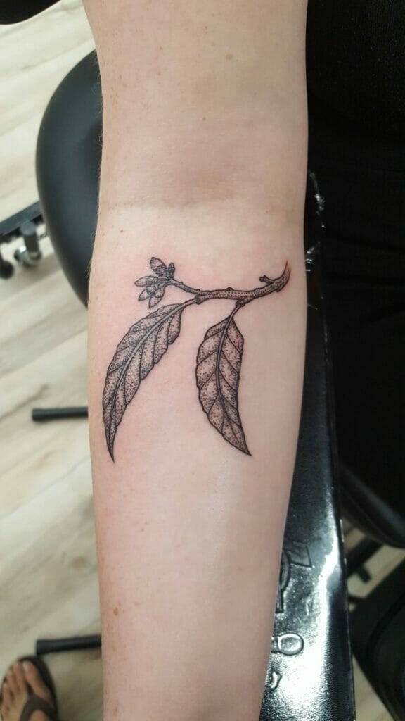 A forearm tattoo depicting a branch with two leaves and a small flower bud.