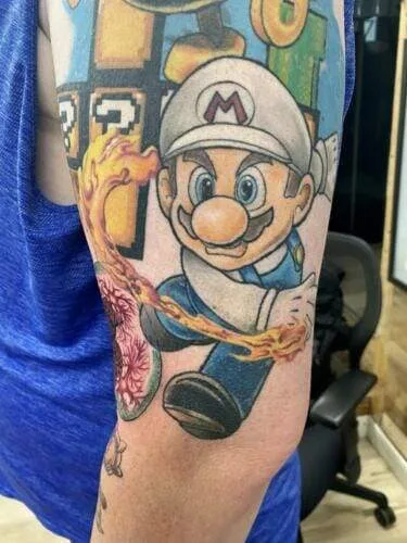 Tattoo of a cartoon character dressed in overalls and a hat on a person's upper arm, with vibrant colors and flame details.