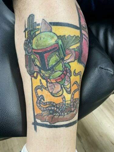 Colorful tattoo of a character in green armor and red helmet, holding a weapon, with tentacles below. The design has a yellow and orange background.