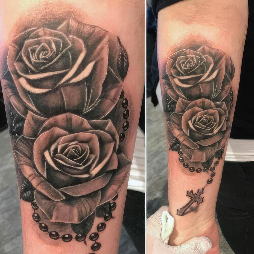 A black and gray tattoo of two roses with leaves and a rosary wrapped around them, featuring a cross pendant, on a person's forearm.