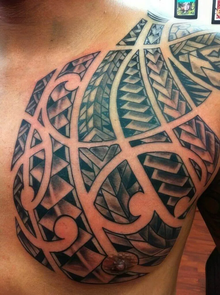Close-up of a chest and shoulder tattoo with a geometric and tribal design featuring bold, symmetrical patterns in black ink.