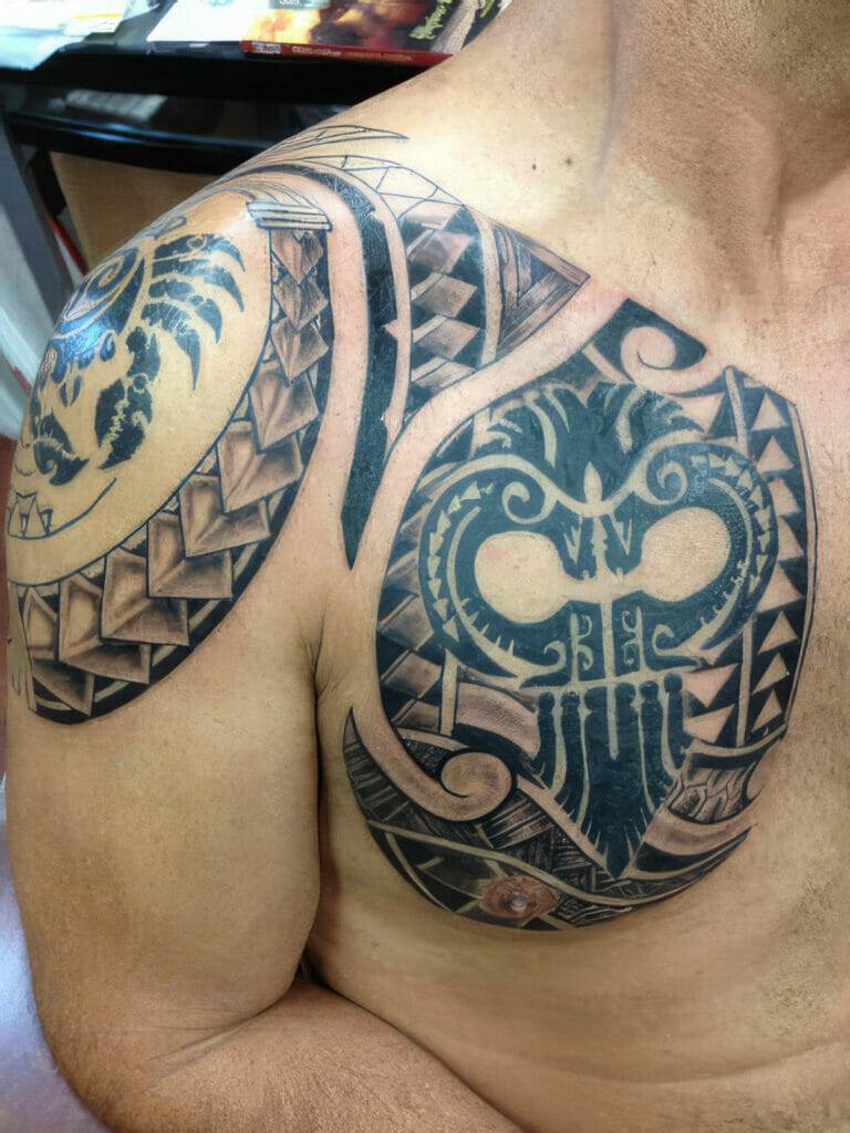 A man's upper chest and shoulder are adorned with intricate black tribal tattoos, including geometric patterns and a prominent owl-like design.