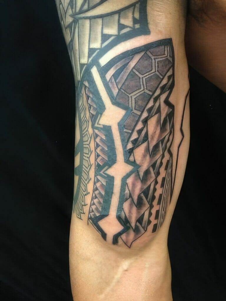 Close-up of an arm tattoo featuring geometric patterns and intricate designs in black ink, covering a portion of the upper arm.