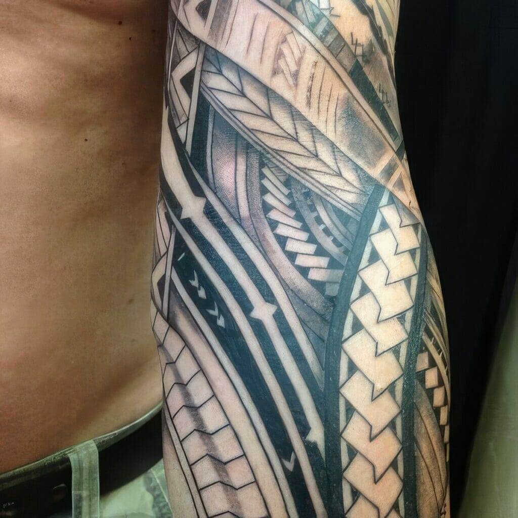 Close-up of a person's arm covered with an intricate, geometric black and grey tattoo design featuring various patterns and shapes.