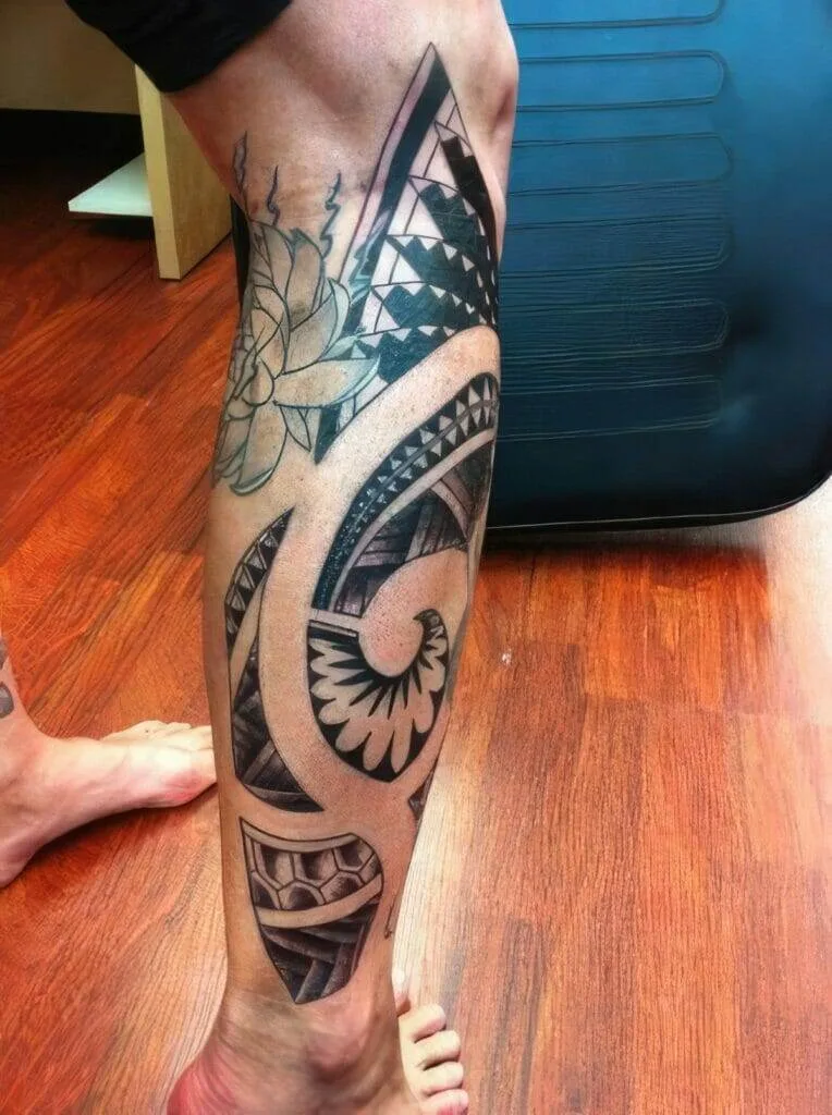 A leg with an intricate tattoo featuring geometric patterns, a flower, and a shell design, on a wooden floor background.