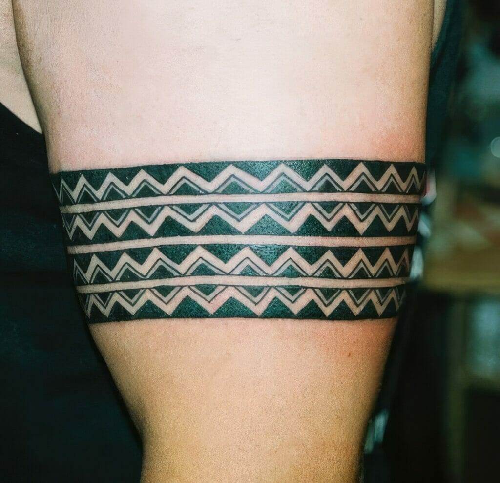 A person's upper arm has three horizontal black bands, each patterned with white triangles in a zigzag design.