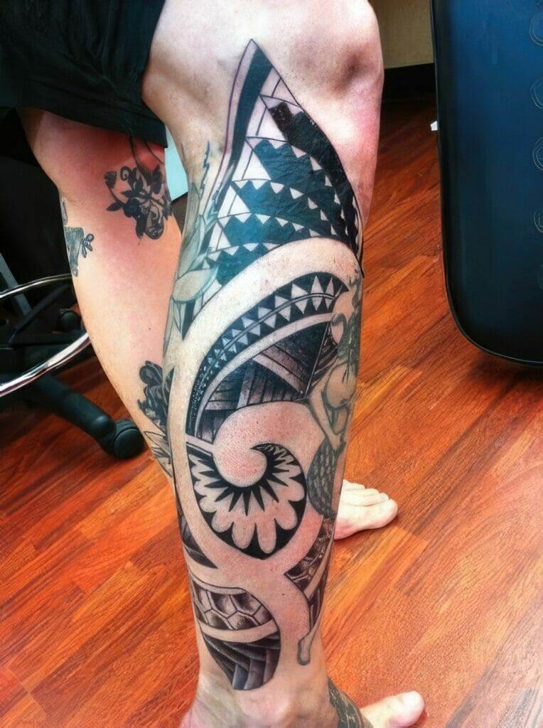 A person with a large, detailed black tribal tattoo covering their lower leg. The tattoo features geometric patterns and intricate designs.
