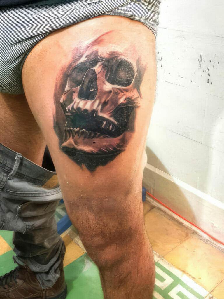 A person's thigh with a detailed tattoo of a human skull in black and grey ink.