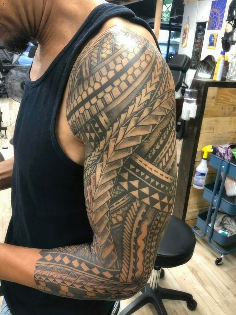 A person wearing a sleeveless shirt reveals an arm covered in a detailed, geometric tribal tattoo sleeve.