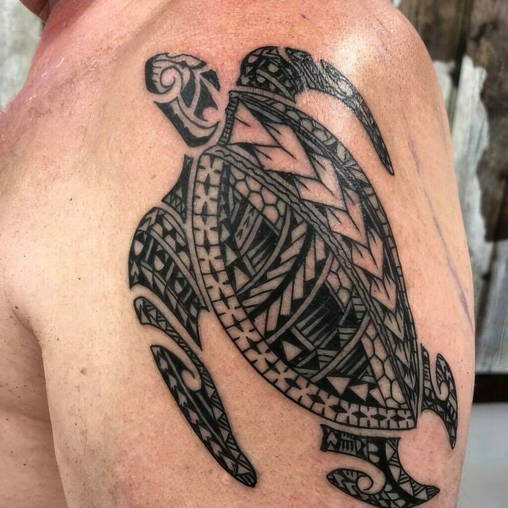 A black and grey tribal-style sea turtle tattoo on an individual's upper arm and shoulder.