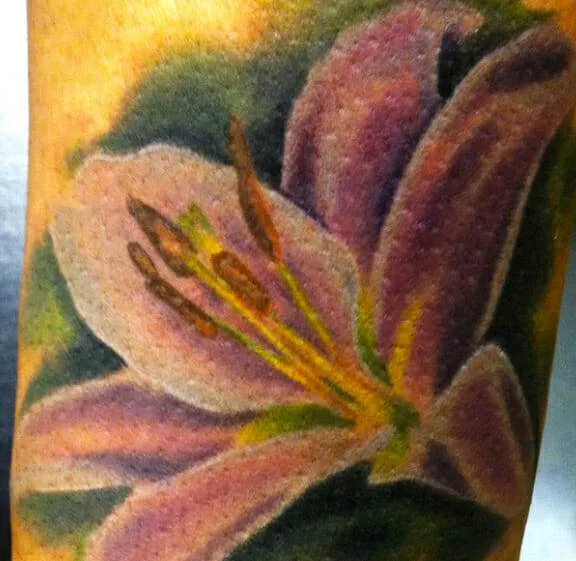 A detailed tattoo featuring a purple lily flower with yellow stamens on a person's skin.
