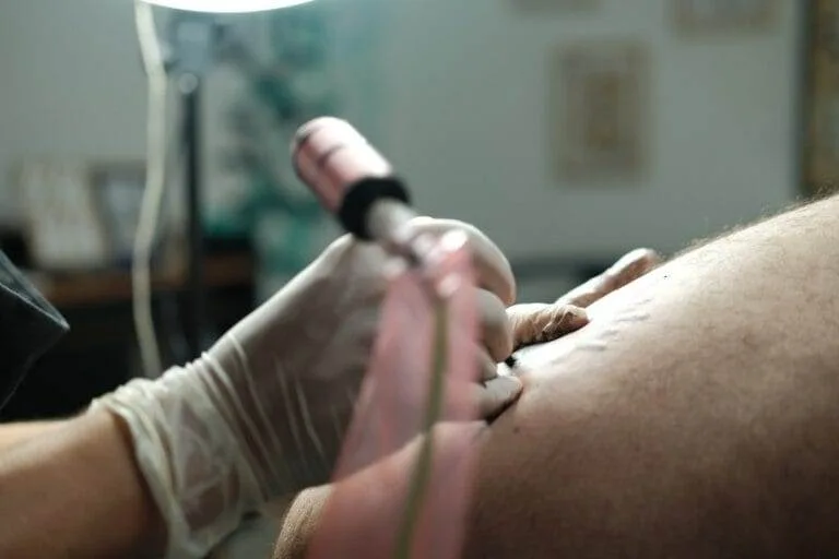 A tattoo artist wearing gloves is tattooing a design on a person's skin using a tattoo machine.