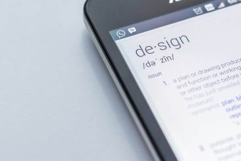 Close-up of a smartphone screen displaying the definition of the word "design" with a white background and part of the phone visible.