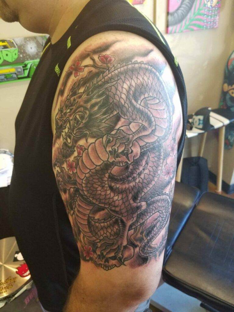 A detailed tattoo of a dragon with cherry blossoms is displayed on a person's upper arm.