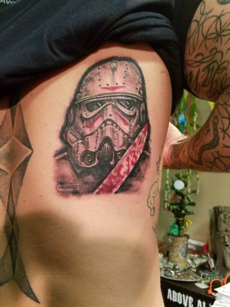 A person with a detailed tattoo of a stormtrooper helmet with a red slash on their ribcage.
