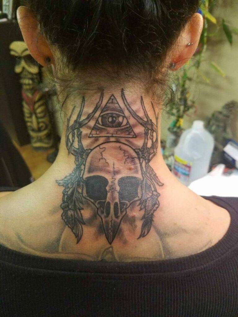 A person with a tattoo on the back of their neck featuring a bird skull, feathers, antlers, and an eye inside a triangle.