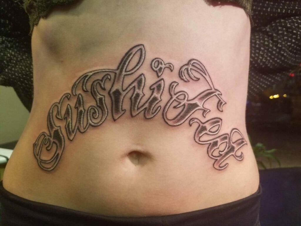 A tattoo on a person's lower abdomen displaying the phrase "Sushi Fest" in ornate script.