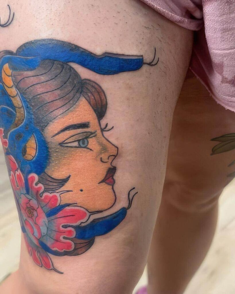 A close-up of a colorful tattoo on a person's thigh depicting a woman's face with blue hair and a flower at the base.