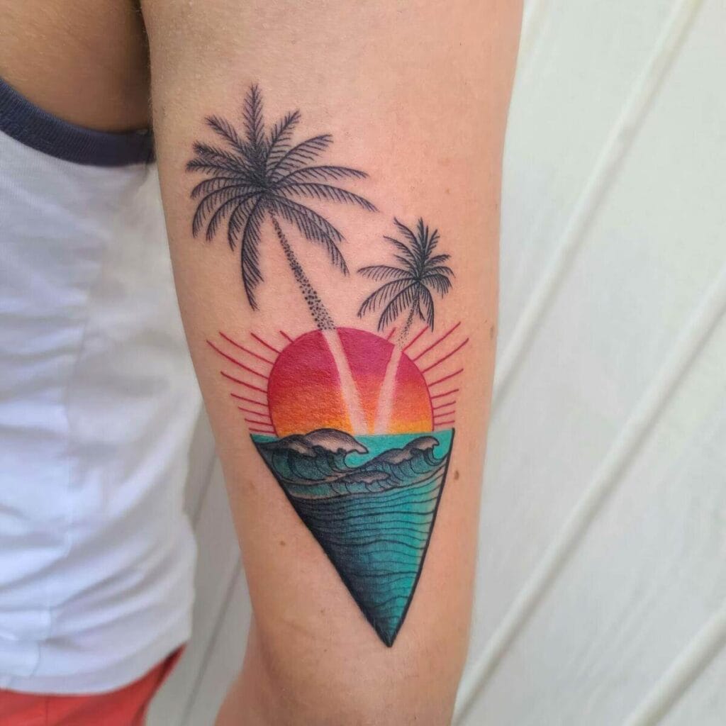Tattoo of a colorful sunset with palm trees and ocean waves contained within an inverted triangle on a person’s upper arm.