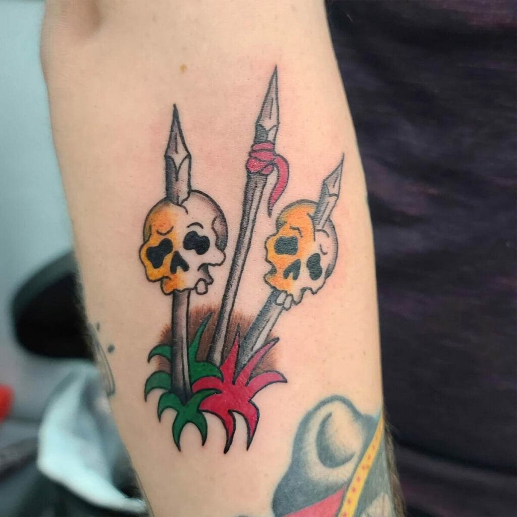 Tattoo of three spears piercing skulls with red and green leaves at the base on a person's arm.