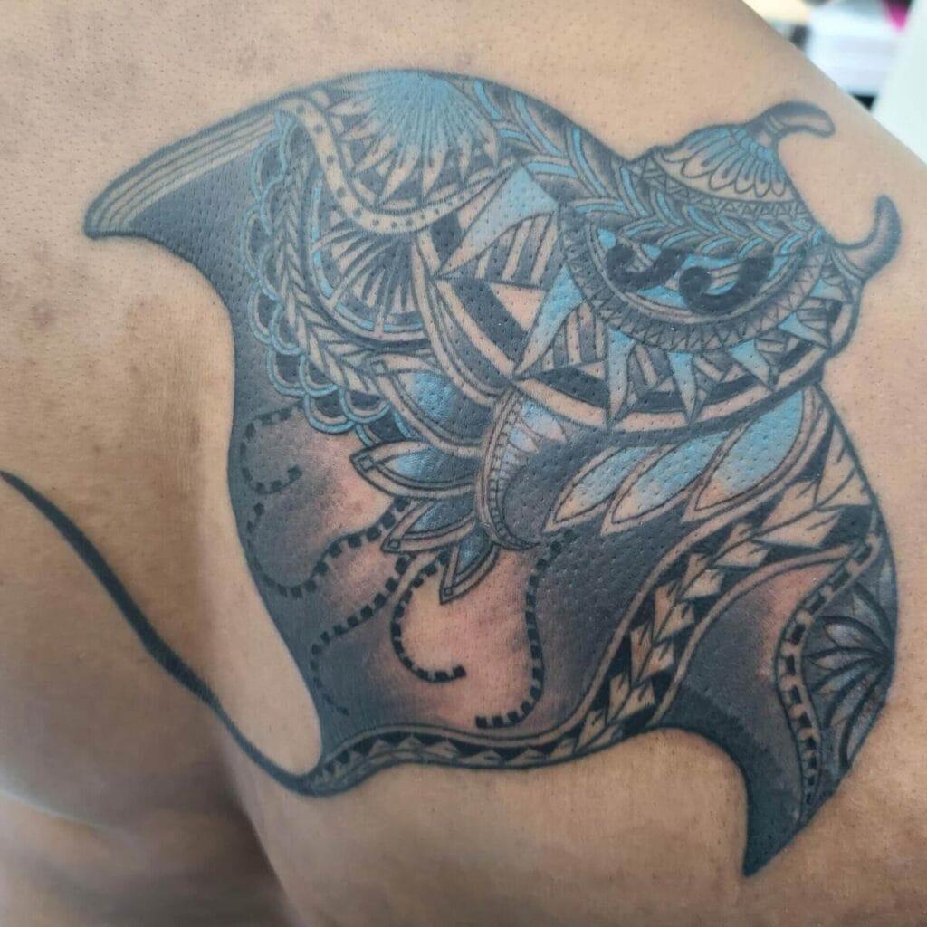 A detailed tattoo on skin features a manta ray with intricate blue and black geometric patterns.
