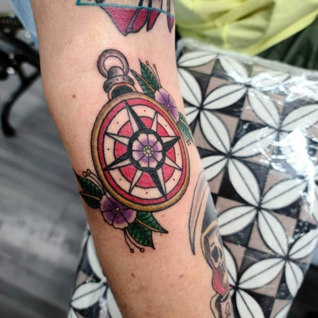 A colorful tattoo of a compass with flowers and leaves on a person's forearm.