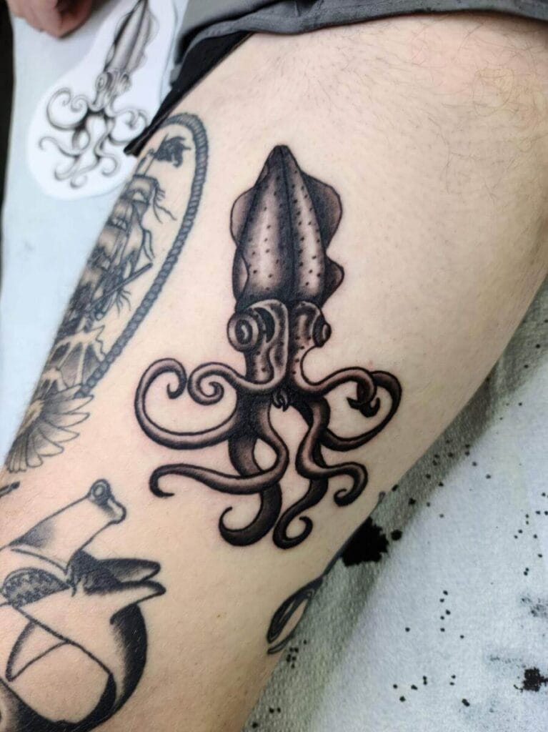 A tattoo of a squid inked on a person's thigh, surrounded by other tattoos.