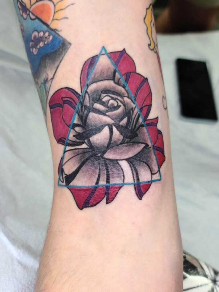 A black and white rose tattoo with red petals enclosed in a blue triangle is inked on a person's forearm.