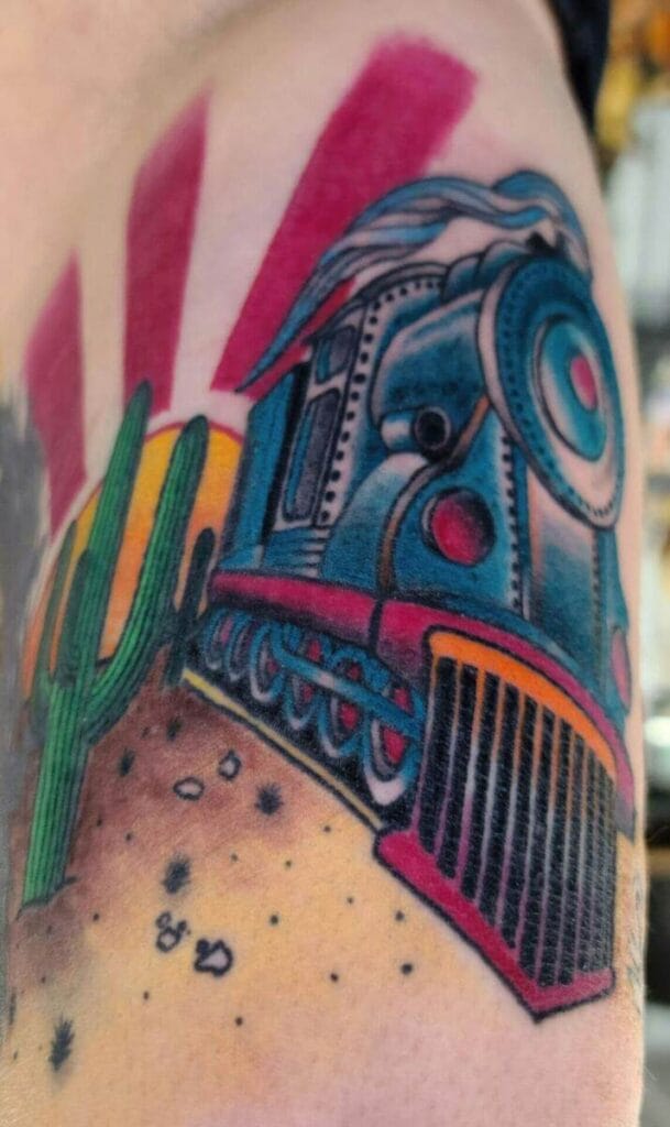 Colorful tattoo of a steam locomotive with a red and pink striped background, a cactus in the foreground, and desert terrain at the bottom.