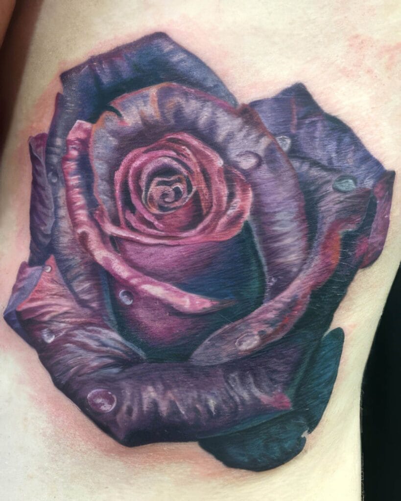 A close-up image of a realistic tattoo depicting a rose, showcasing detailed petals and water droplets. The design features shades of purple, pink, and dark blue.