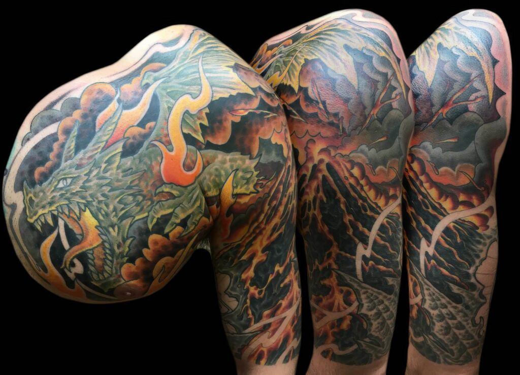 Detailed tattoo of a dragon enveloped in flames and smoke, spanning the entire back and arms of the individual. The design is vibrant with intricate patterns and shading.