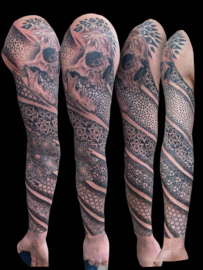 A full sleeve tattoo covering an entire arm, featuring intricate geometric patterns, floral designs, and a human skull.