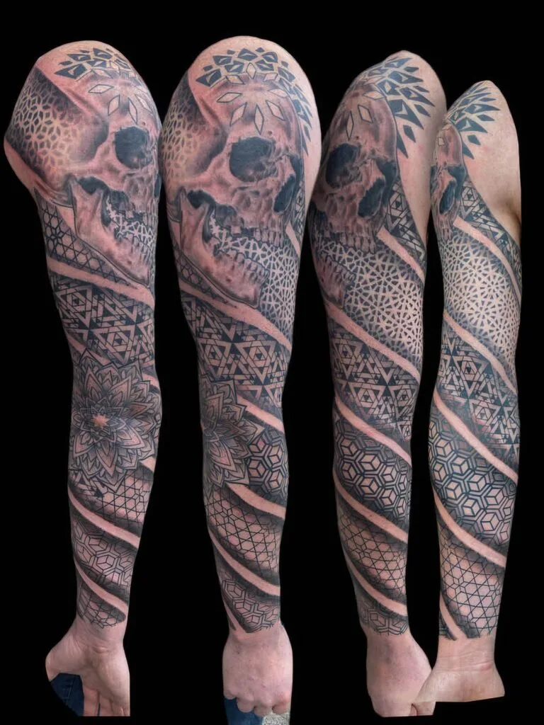 A full sleeve tattoo covering an entire arm, featuring intricate geometric patterns, floral designs, and a human skull.